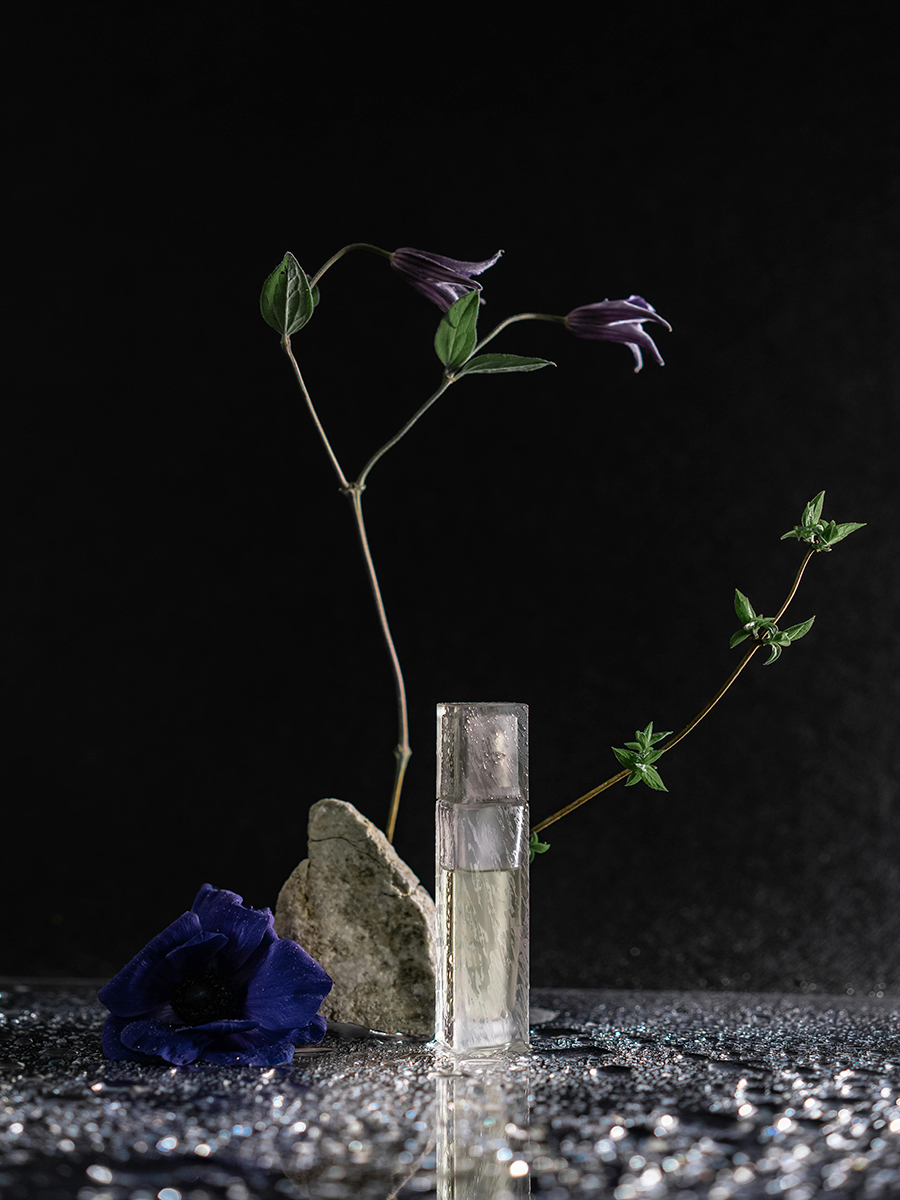 perfume bottle with stones and flower with water splash around